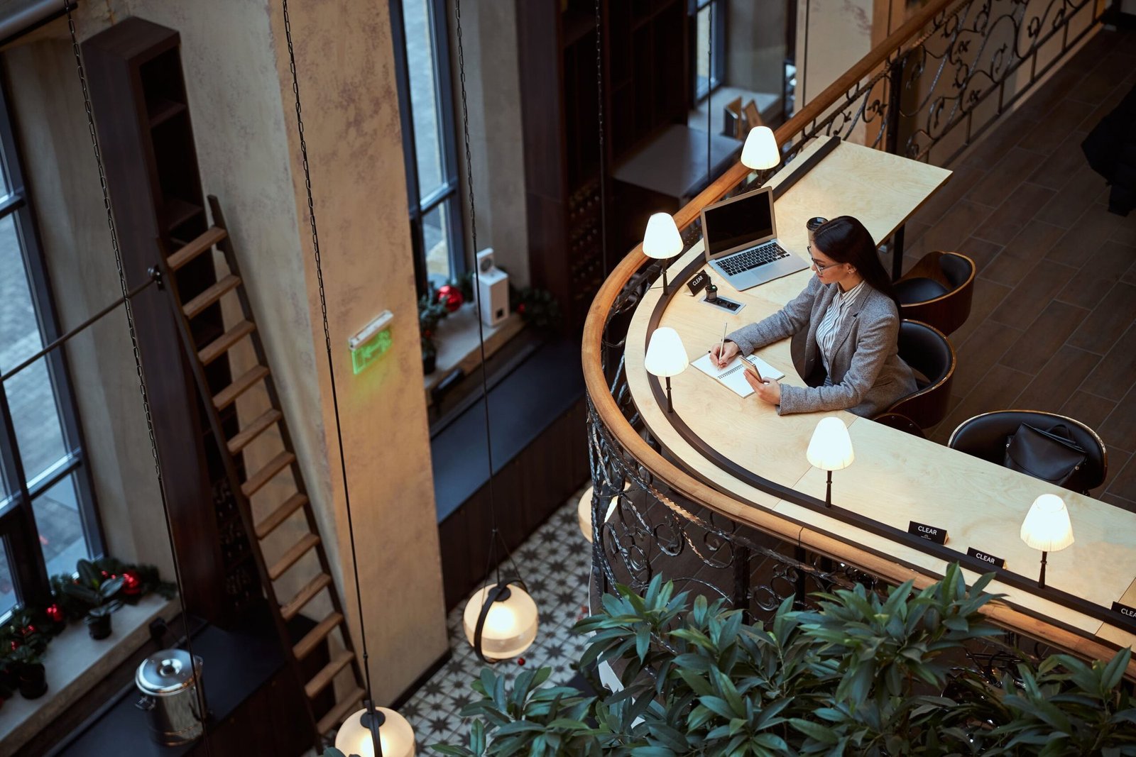 Vista cenital de la recepción de un hotel: una huésped trabajando con su portátil en el mostrador