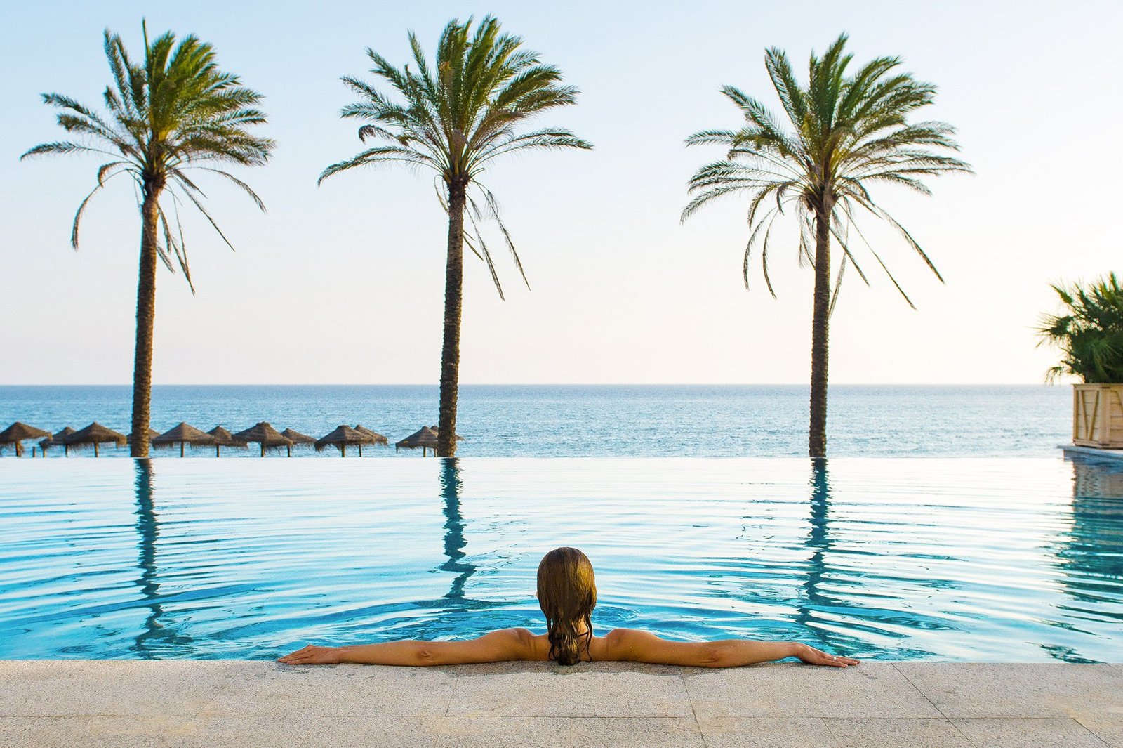 Huésped contemplando el mar desde una piscina infinita entre palmeras