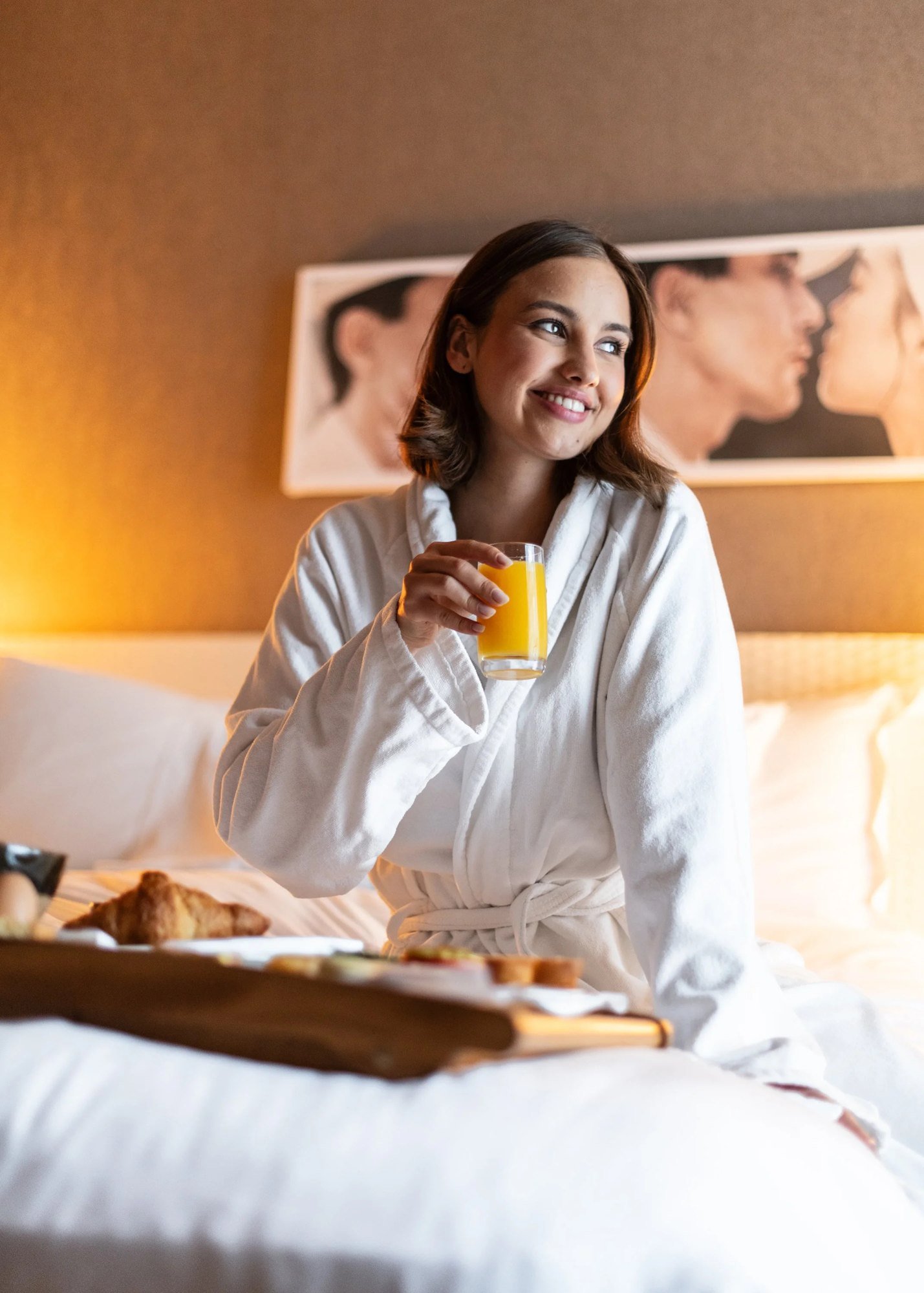 Pies descalzos sobre la cama sujetando un café, mientras alguien abre las cortinas al fondo